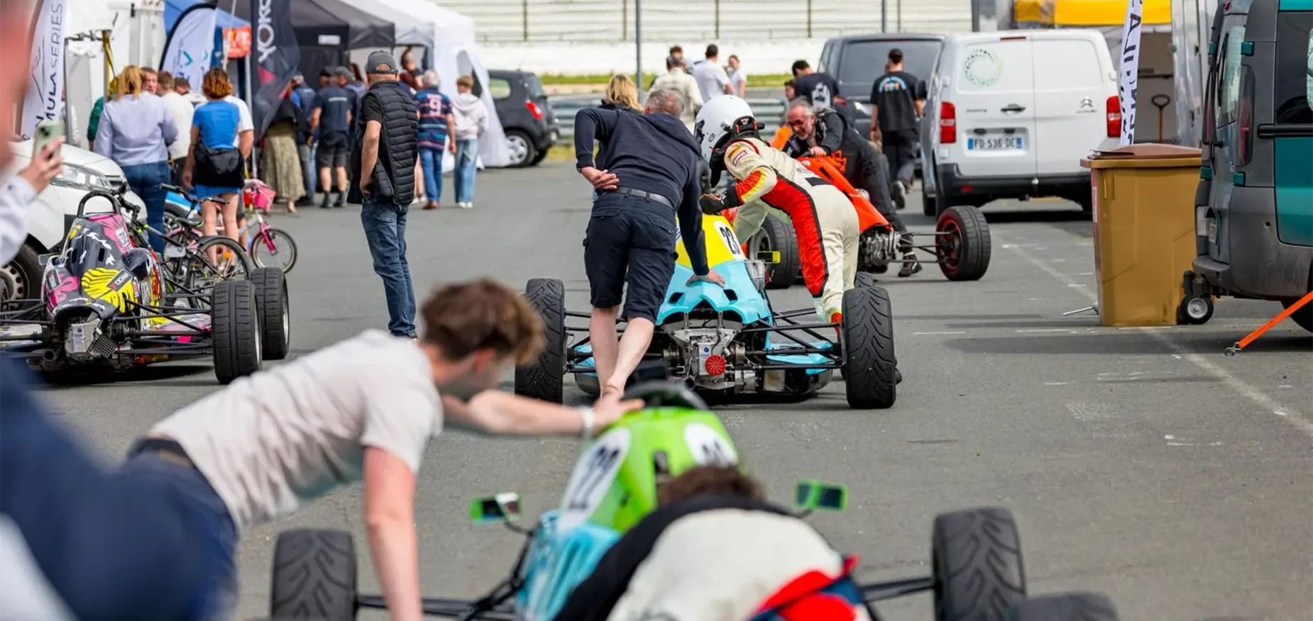 passer-du-karting-a-la-monoplace-formule-ford-paddock Pilotes en paddock poussant leurs Formule Ford vers la pré-grille avant une séance en championnat